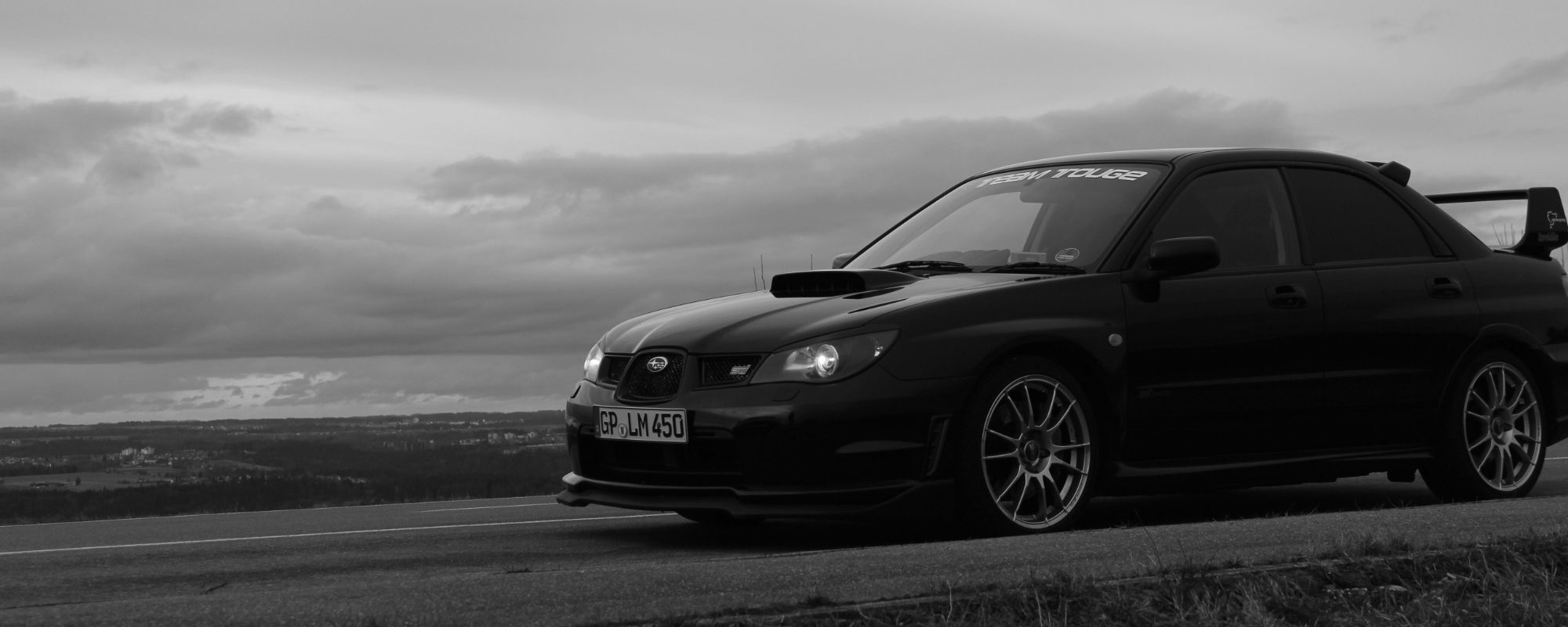 Schwarzer Sportwagen im Focus, vor dramatischem Himmel in Schwarz-Weiß.